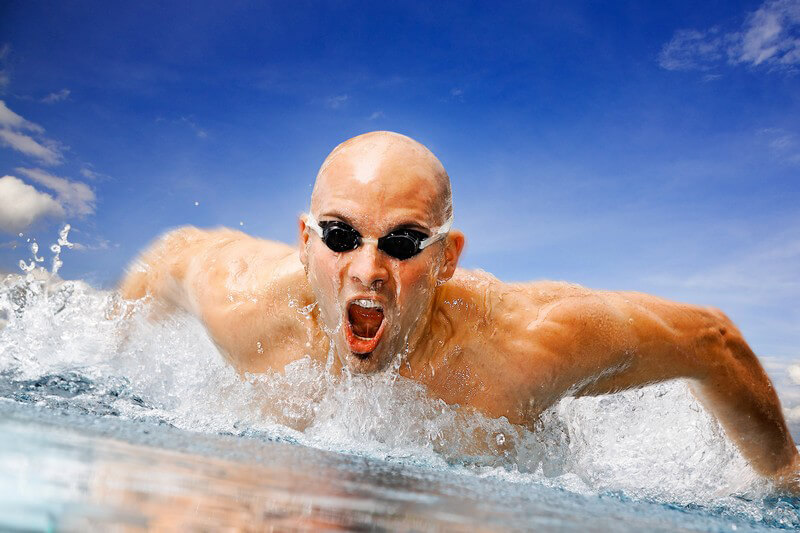 Muskulöser Mann mit Taucherbrille beim Schwimmen unter blauem Himmel