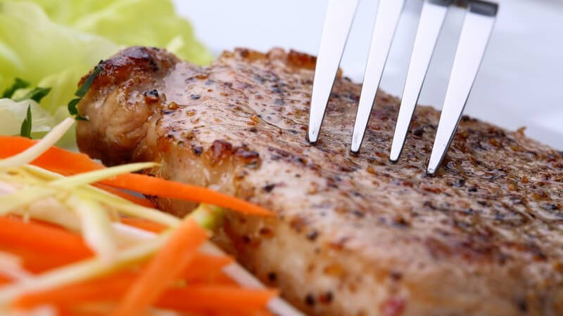 Gabel auf einem Steak und etwas roter und grüner Salat