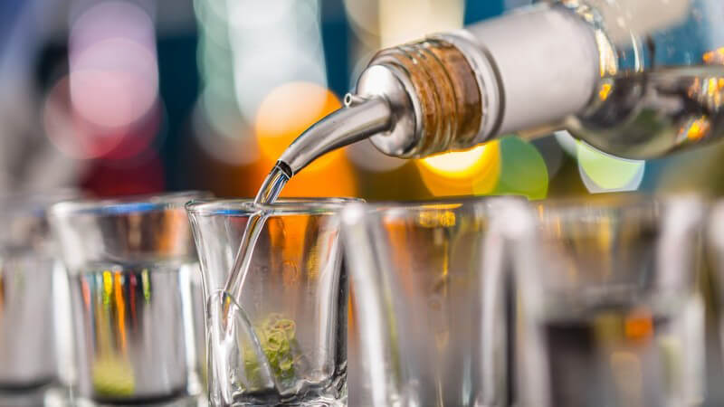 Eine Reihe von Schnapsgläsern wird an einer Bar mit klarem Schnaps befüllt