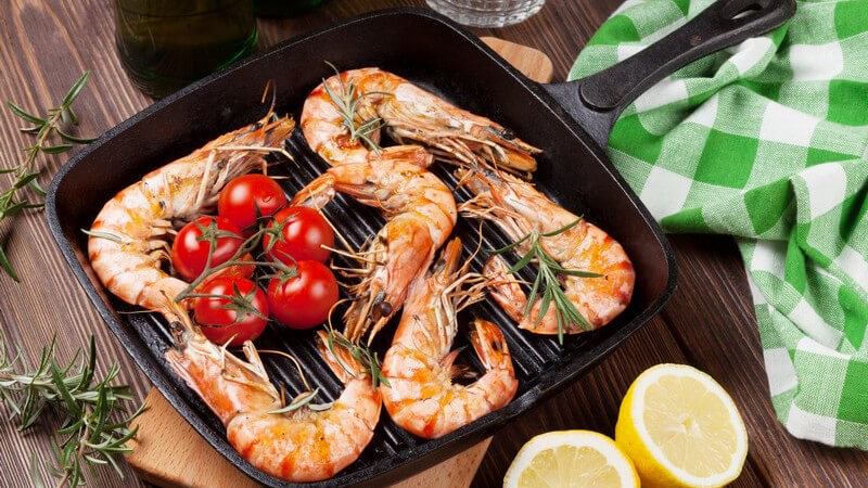 Schwarze Gusseisenpfanne mit gebratenen Garnelen, Kirschtomaten und Rosmarin