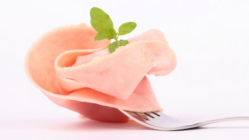 Scheibe gekochter Schinken mit frischen Kräutern auf Gabel gepickt, weißer Hintergrund