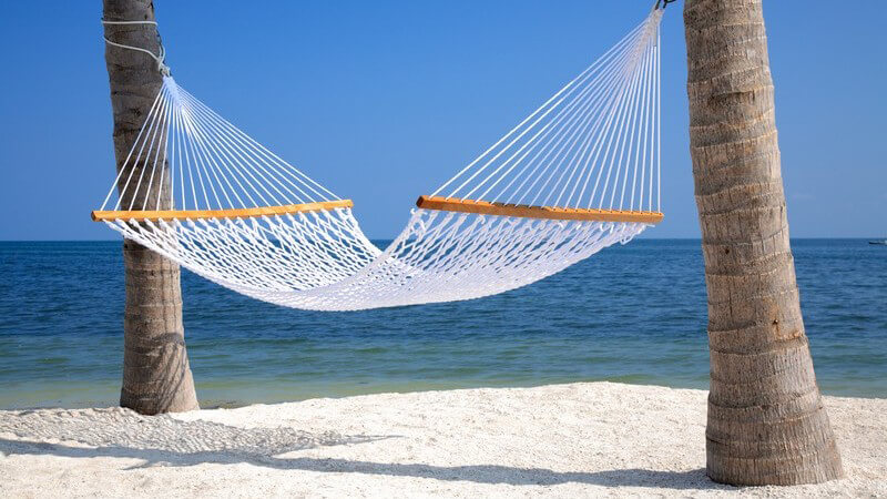 Weiße Hängematte zwischen zwei Palmen am weißen Sandstrand mit blauem Meer und blauem Himmel