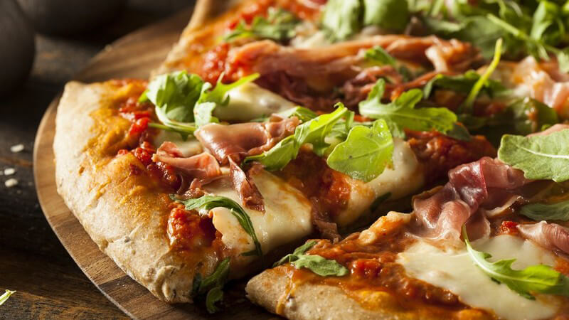 Geschnittene Pizza mit Schinken und Rucola auf Holzteller