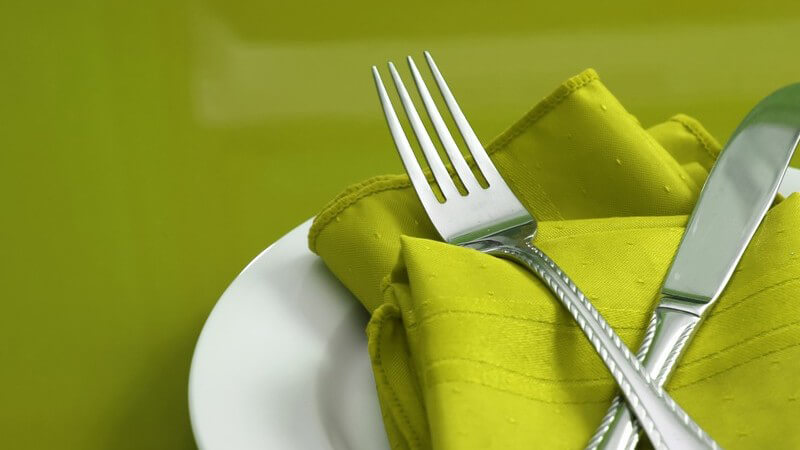 Besteck auf grüner Serviette auf weißem Teller, grüner Hintergrund