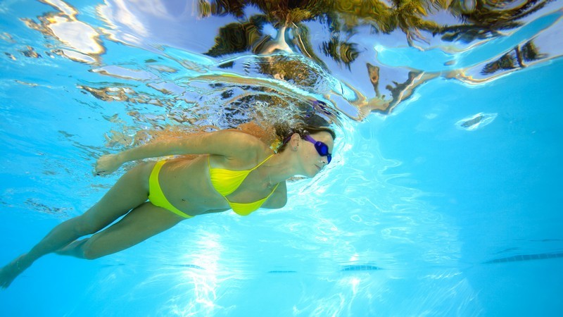 Unterwasseraufnahme: Frau im Bikini schwimmt unter Wasseroberfläche, Himmel mit Palmen