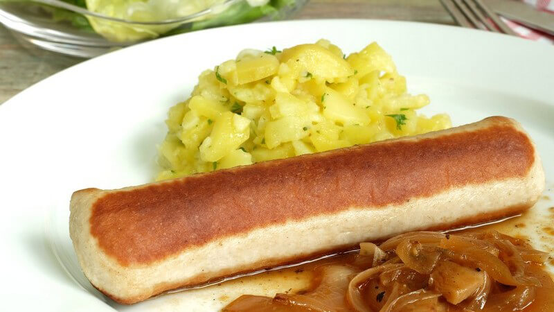 Oberländer Wollwurst mit Kartoffelsalat und Zwiebelsauce auf einem Teller