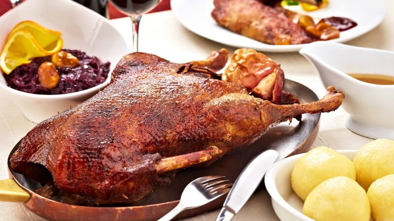 Gebratene Gans in langer Pfanne auf Festtafel neben Klößen, Soße und Rotkohl