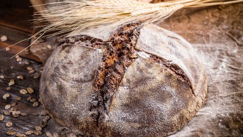 Getreideähren liegen auf einem großen runden Landbrot voller Mehl