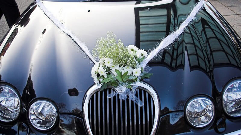 Blumenstrauß auf Haube einer schwarzen Limousine bei Hochzeit