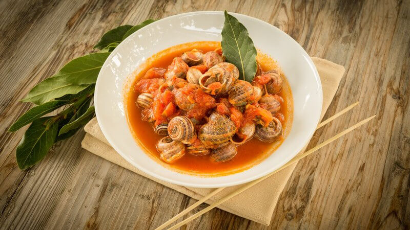 Teller mit Schnecken in Tomatensoße neben Essstäbchen auf Holztisch