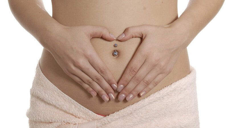 Nackter Bauch einer Frau, sie umrahmt Bauchnabel in Herzform mit Händen