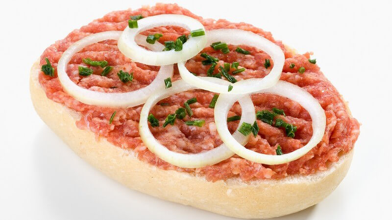 Halbes Brötchen mit Mettwurst, Zwiebelringen und Petersilie auf weißem Hintergrund