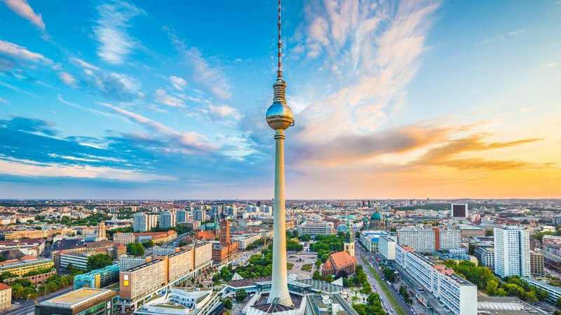 Blick über Berlin mit dem Fernsehturm im Zentrum unter blauem, wolkigem Himmel bei Sonnenuntergang