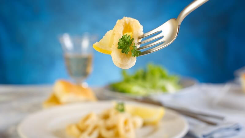 Gabel mit Tintenfischring, im Hintergrund Teller auf Tisch