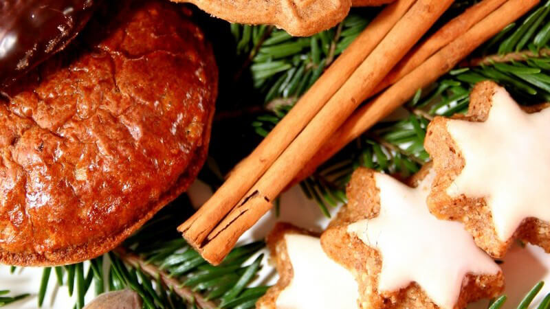 Diverse Weihnachtsplätzchen neben Zimtstangen und Haselnüssen auf Tannenzweig