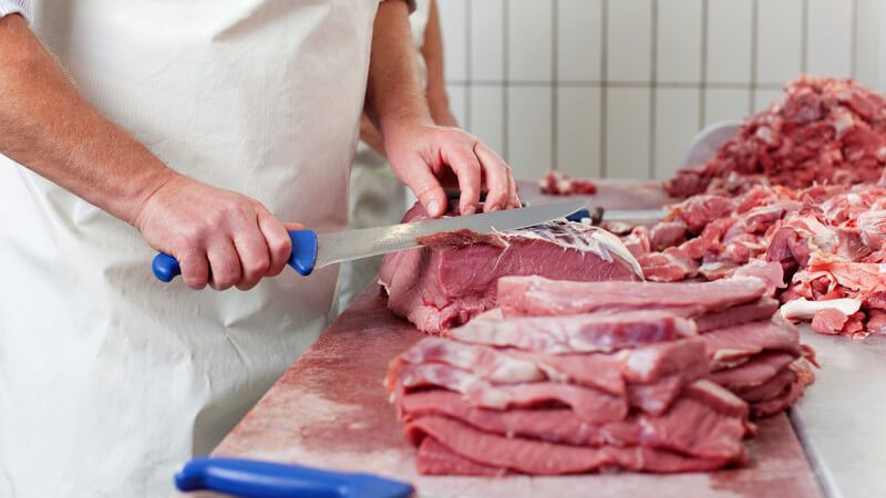 Metzgerei - Hände eines Metzgers, er schneidet Fleisch klein