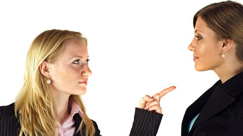 Blonde Frau mit offenen Haaren zeigt drohend auf brünette Frau mit zurückgesteckten Haaren