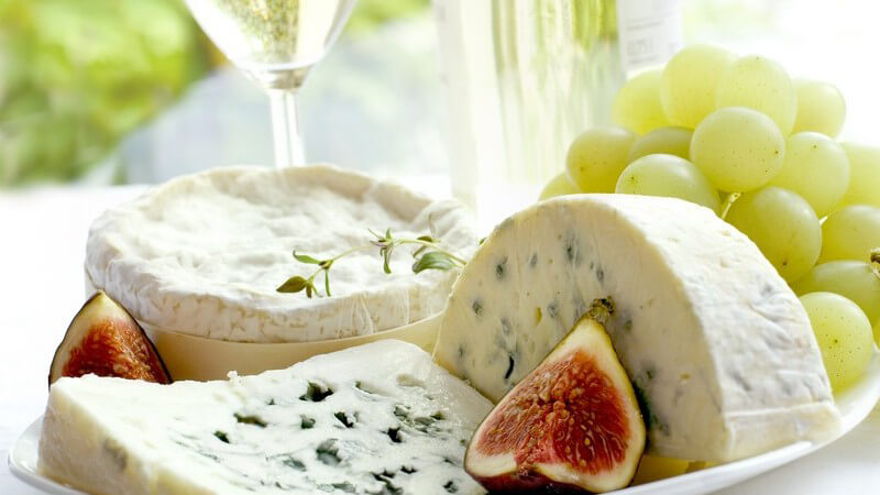 Nahaufnahme Käseteller mit Trauben, daneben Glas mit Wein