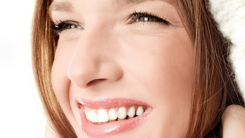 Rot-brünette Frau lächelt mit gekniffenen Augen, hält mit beiden Händen ihre weiße Kapuze am Kinn fest