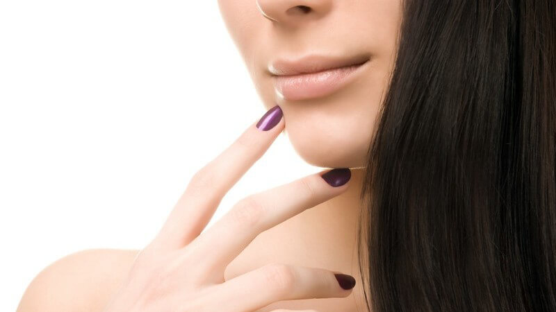 Untere Gesichtshälfte einer jungen Frau, hält zwei Finger mit lilanem Nagellack ans Kinn