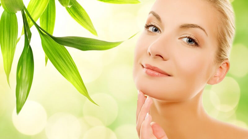 Junge Frau streicht sich übers Kinn, neben ihr grüne Pflanze