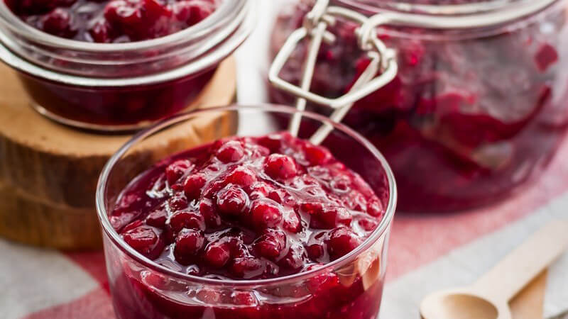 Gläser mit eingemachten Preiselbeeren, daneben zwei kleine Holzlöffel