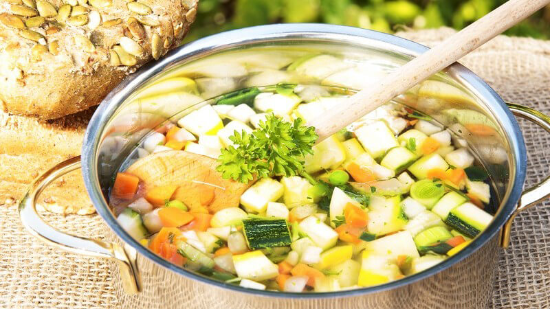 Topf mit Gemüsesuppe neben Körnerbrötchen