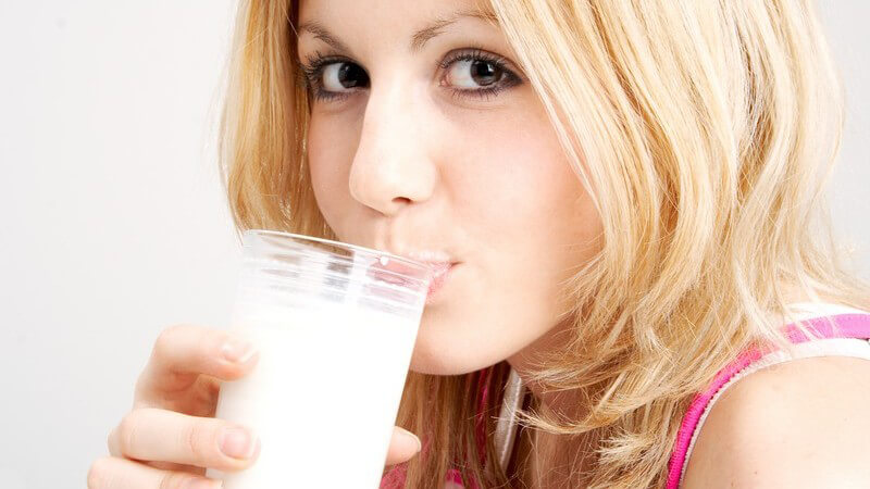 Blondes Mädchen mit rosa Spaghettiträgern trinkt aus einem Glas Milch