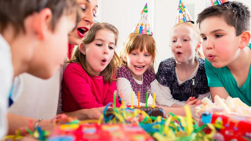 Frau und Kinder einer Geburtstagsparty pusten die Kerzen auf einem Kuchen aus