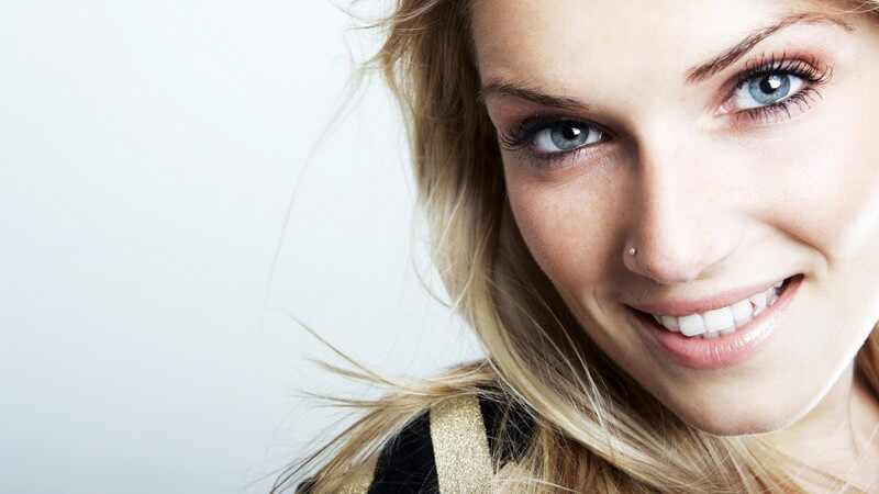Blonde junge Frau mit blauen Augen und Nasenpiercing lächelt in Kamera