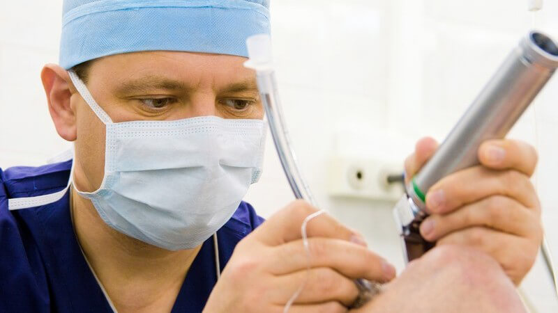 Operation Arzt Chirurg mit Haube und Mundschutz bearbeitet Knie, heller Raum, medizinische Instrumente