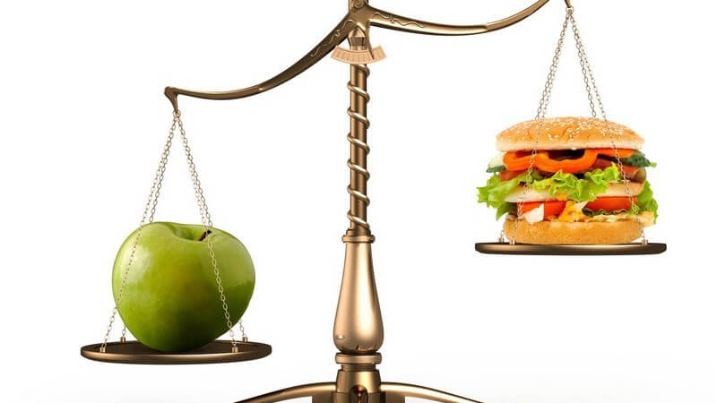 Grüner Apfel und Hamburger auf Waage