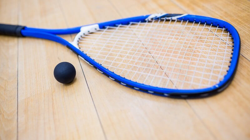 Blauer Squashschläger und Squashball auf Holzboden