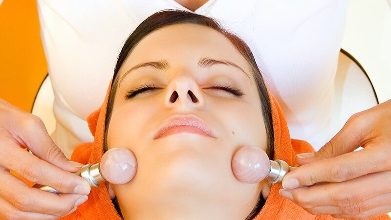 Gesicht einer jungen Frau, sie bekommt Gesichtsmassage mit kleinen Steinen