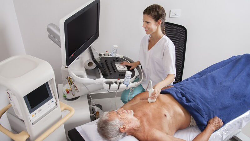 Junge Ärztin untersucht den Brustkorb eines alten Mannes per Ultraschall