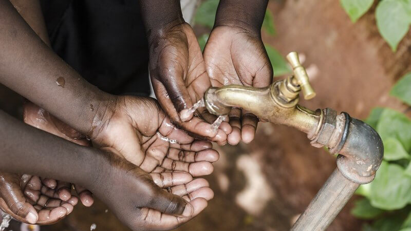 Dunkelhäutige Kinderhände unter einem Wasserhahn