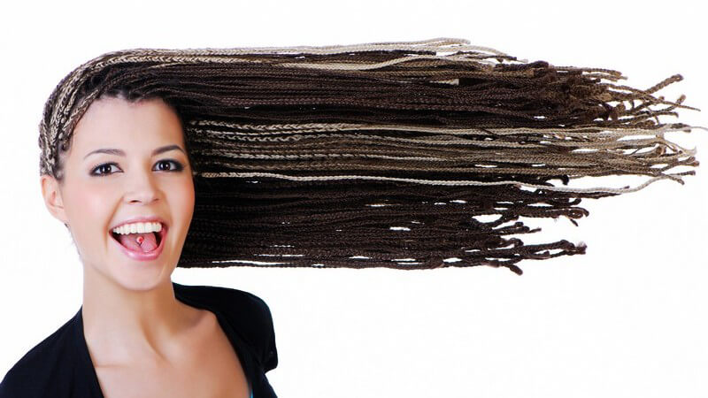 Braun-blonde Rastazöpfe junger Frau mit Zungenpiercing werden zur Seite geweht