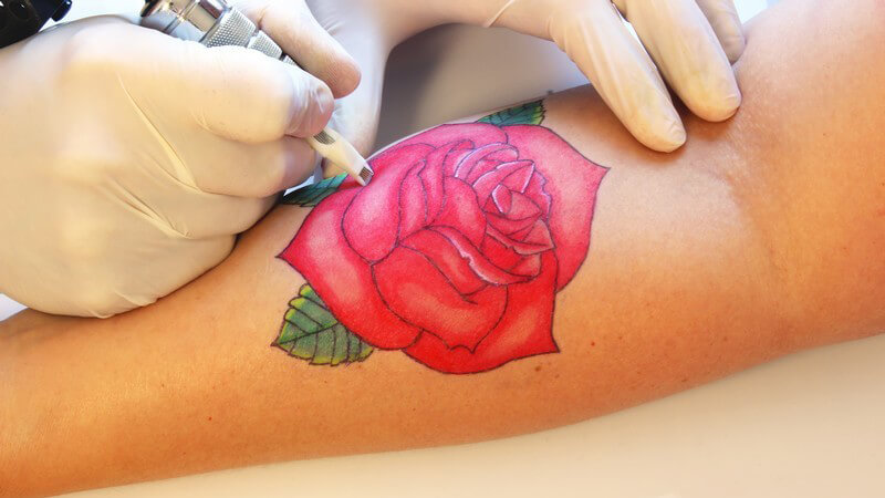 Tätowierer tätowiert eine große rote Rose auf einen Unterarm