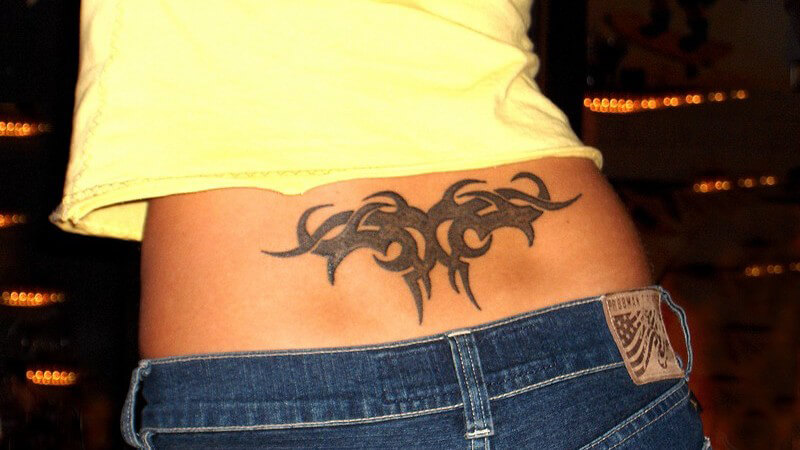 Rückenansicht, Frau in Jeans und bauchfreiem Top, Tribal Tattoo über dem Po