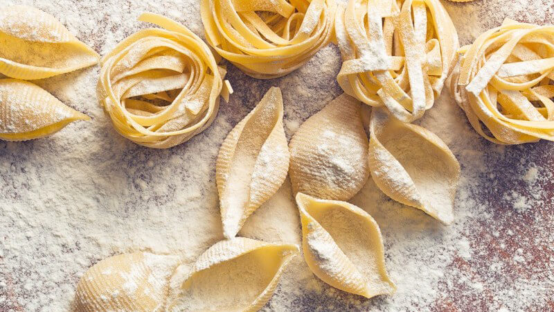 Rohe und mit Mehl bestäubte Muschel- und Bandnudeln