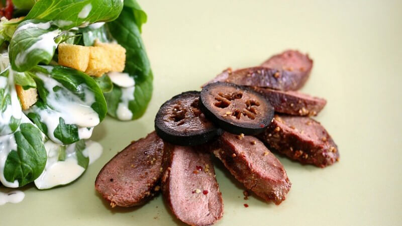 Wildfilet aus Hasenfleisch auf mintgrüner Fläche mit Feldsalat, Croutons und Joghurt-Dressing an der linken Seite