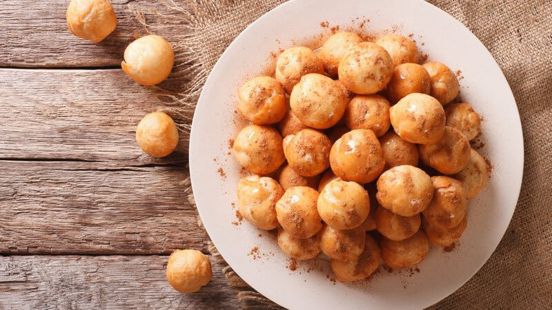 Loukoumades mit Honig und Zimt auf weißem Teller auf einem Holztisch