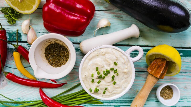 Türkisfarbener Tisch voller Zutaten für die Vorspeise "Melitzanosalata" wie Aubergine, Knoblauch, Peperoni und Zitrone