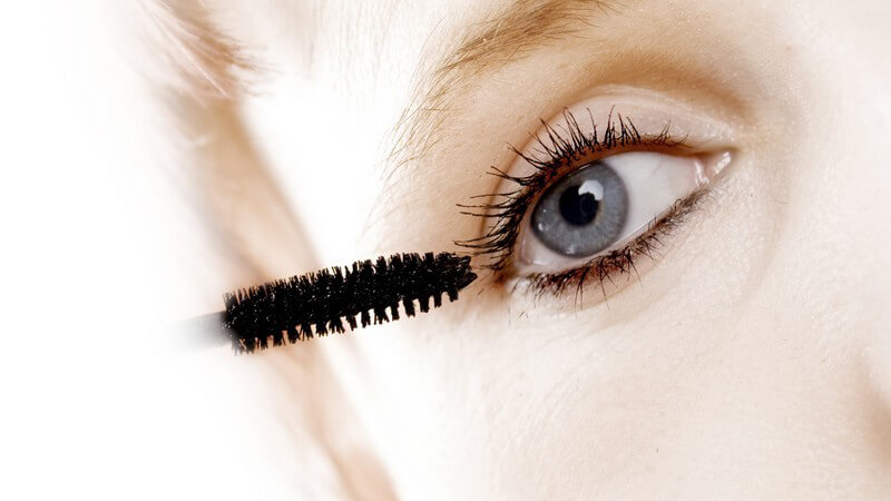 Nahaufnahme blonde Frau mit blauen Augen beim Schminken mit Mascara oder Wimperntusche