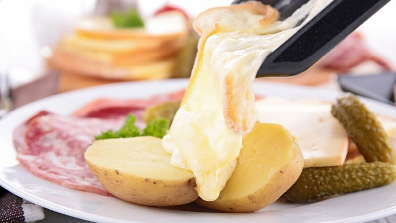 Raclette - Käse wird von Raclette Pfanne auf Teller gelegt