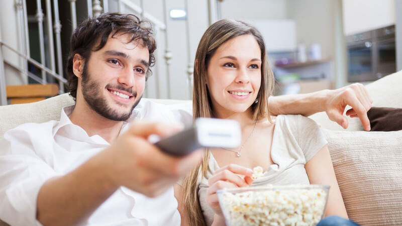 Paar guckt Fernsehen, er hält die Fernbedienung und sie das Popcorn