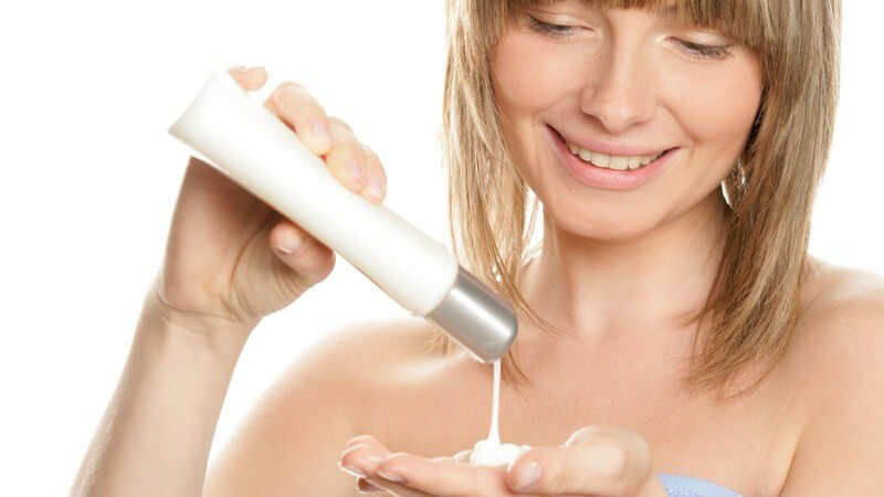 Junge Frau trägt Bodylotion auf Hände auf, weißer Hintergrund