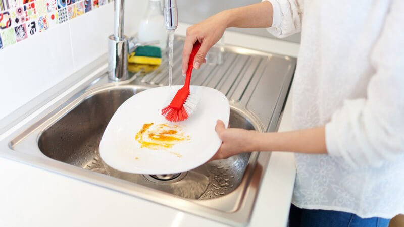 Abwaschen eines Tellers mit roter Bürste über dem Spülbecken