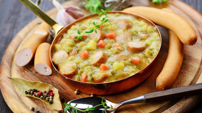 Erbsensuppe mit Bockwürstchen auf rundem Holzteller
