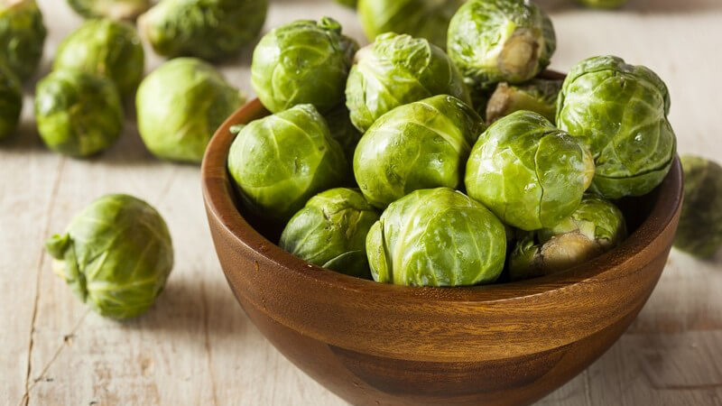 Frischer Rosenkohl in brauner Schüssel auf einem Holztisch